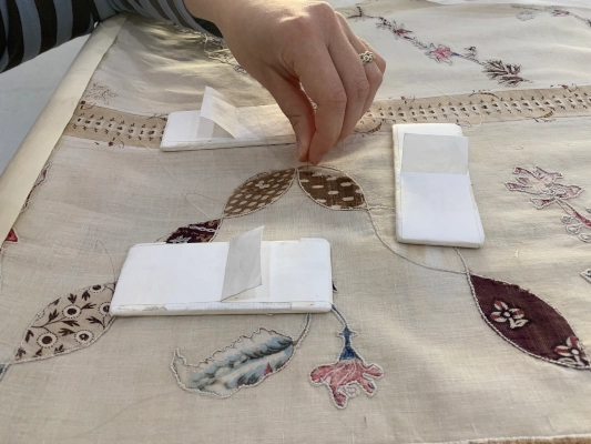 Close up of a conservators hand as they repair the appliqué patches on William Cowper's quilt.