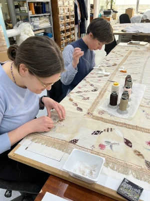 Two conservators at work in the studio repairing the appliqué patches on William Cowper's quilt.