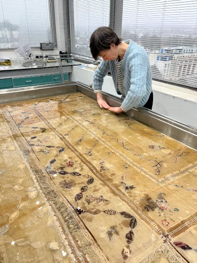 Conservator wet cleaning a historic quilt in a large washbath.