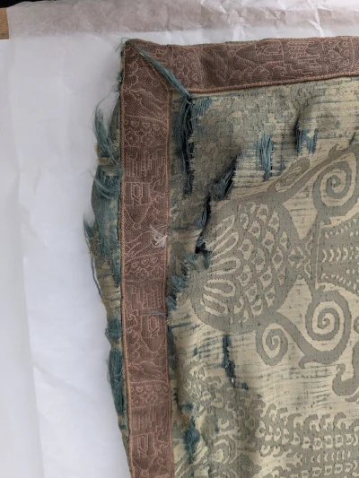 Corner detail of cushion before treatment showing splits in silk damask